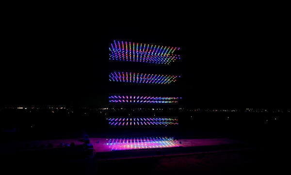 写真：5つの平面を縦に積み重ねたような形状を表現するカラフルに光るドローン群