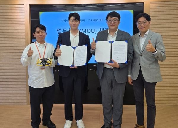 写真：合意書やドローンを持ちサムズアップする4人