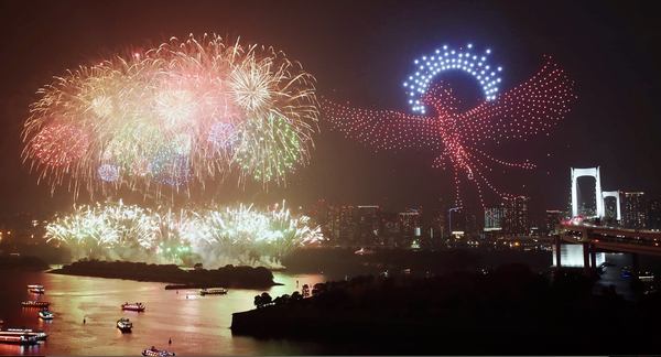 写真：夜空に打ち上がる花火と、火の鳥が描かれたドローンショー