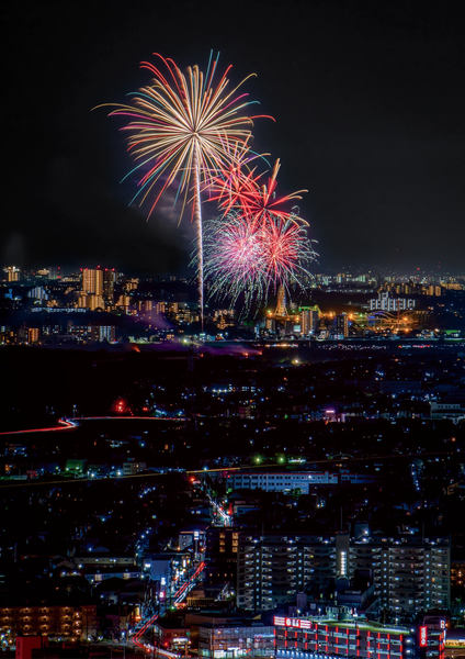 写真:夜景の向こうで打ち上がる花火