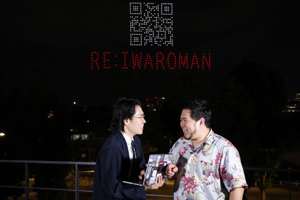 写真：漫才をする2人、上空にドローンショーで描かれたQRコード、「RE：IWAROMAN」