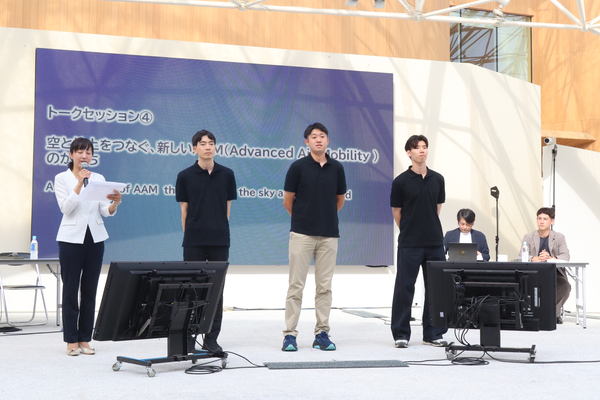 写真：壇上に並ぶ3人、司会者