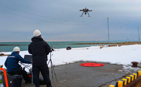 写真：雪が積もる屋外を飛行するドローン、操縦者