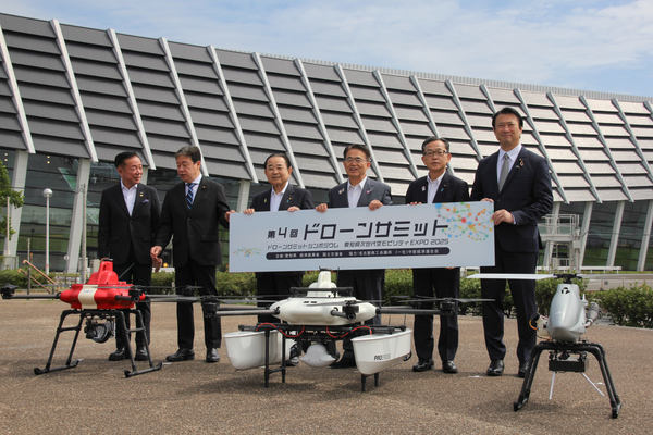 写真：「第4回ドローンサミット」のボードを手に持ち、機体の後ろで横並びになる6人