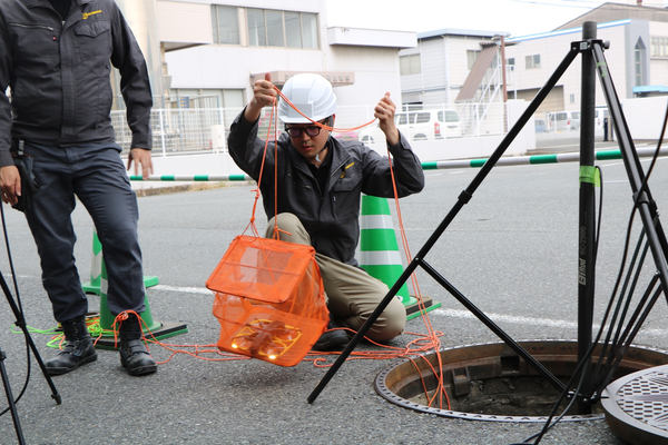 写真：ドローンをロープ付きのメッシュのケースに入れ、マンホールから下水管に下ろす様子
