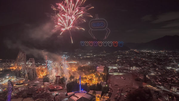 写真：打ち上がる花火と、ドローンショーで遊園地上空に描かれたクレーンゲーム