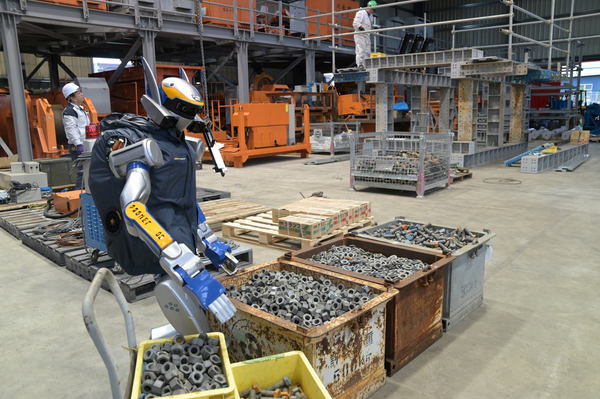 写真：ボルト、ナット、ワッシャーが入ったコンテナ等の傍に立つヒューマノイドロボット