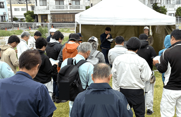 写真：屋外に設置されたテント周辺で説明を行う様子、多数の参加者