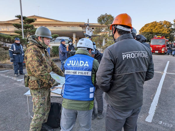 写真：屋外で自衛隊、JUIDA、プロドローンのスタッフが話し合う様子