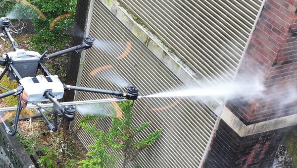 写真：飛行しながら外壁に洗浄剤を噴射するドローン