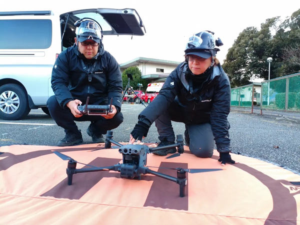 写真:ランディングパッド上のドローンと作業する2人