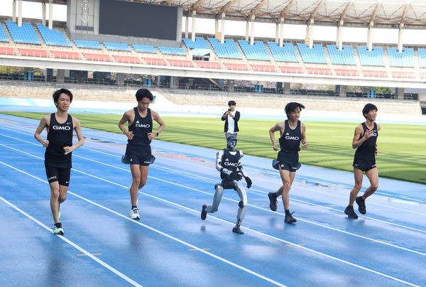 写真：屋外の陸上トラックを走るヒューマノイドロボットとプロアスリートたち