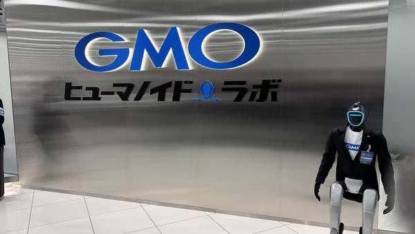 写真：GMOヒューマノイドラボのロゴウォールの前に立つ「ひとみん」