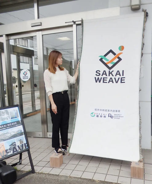 写真：タペストリーと並ぶ女性