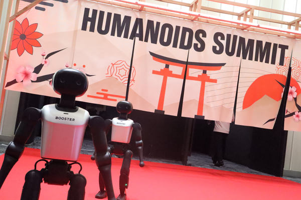写真:鳥居などの日本のモチーフが描かれた「Humanoids Summit」ののれん、ヒューマノイド2体