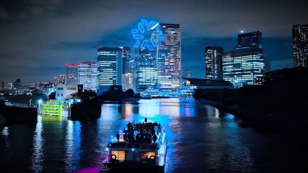写真：航行するナイトクルーズ船の向こう側に見えるドローンショー