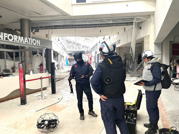 写真：イオンモール熊本の建物内、床に置いたドローン、3人のスタッフ